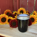 Zanne's Farm Dr Pepper Jelly half pint jar with scattered multicolored sunflowers on rustic wood with red fence background