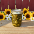 Zanne's Farm Cowboy Candy half pint jar centered with sunflowers and daisies on rustic wood with red fence background