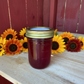 Zanne's Farm Muscadine Jelly half pint jar with scattered multicolored sunflowers on rustic wood with red fence background