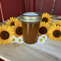 Zanne's Farm Pear Honey half pint jar with scattered sunflowers and daisies on rustic wood with red fence background